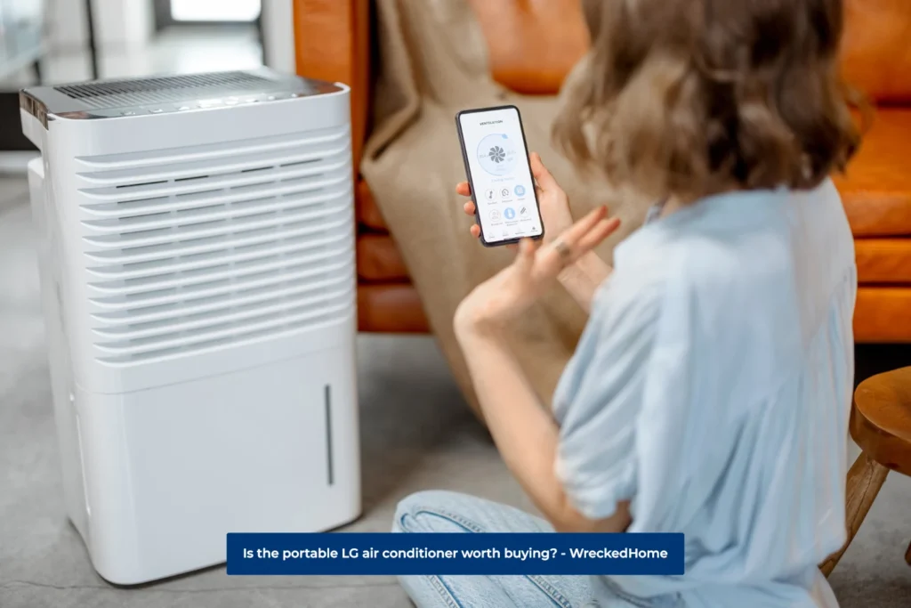 Woman Sitting Beside portable LG air conditioner, using the app on her phone to change the settings.